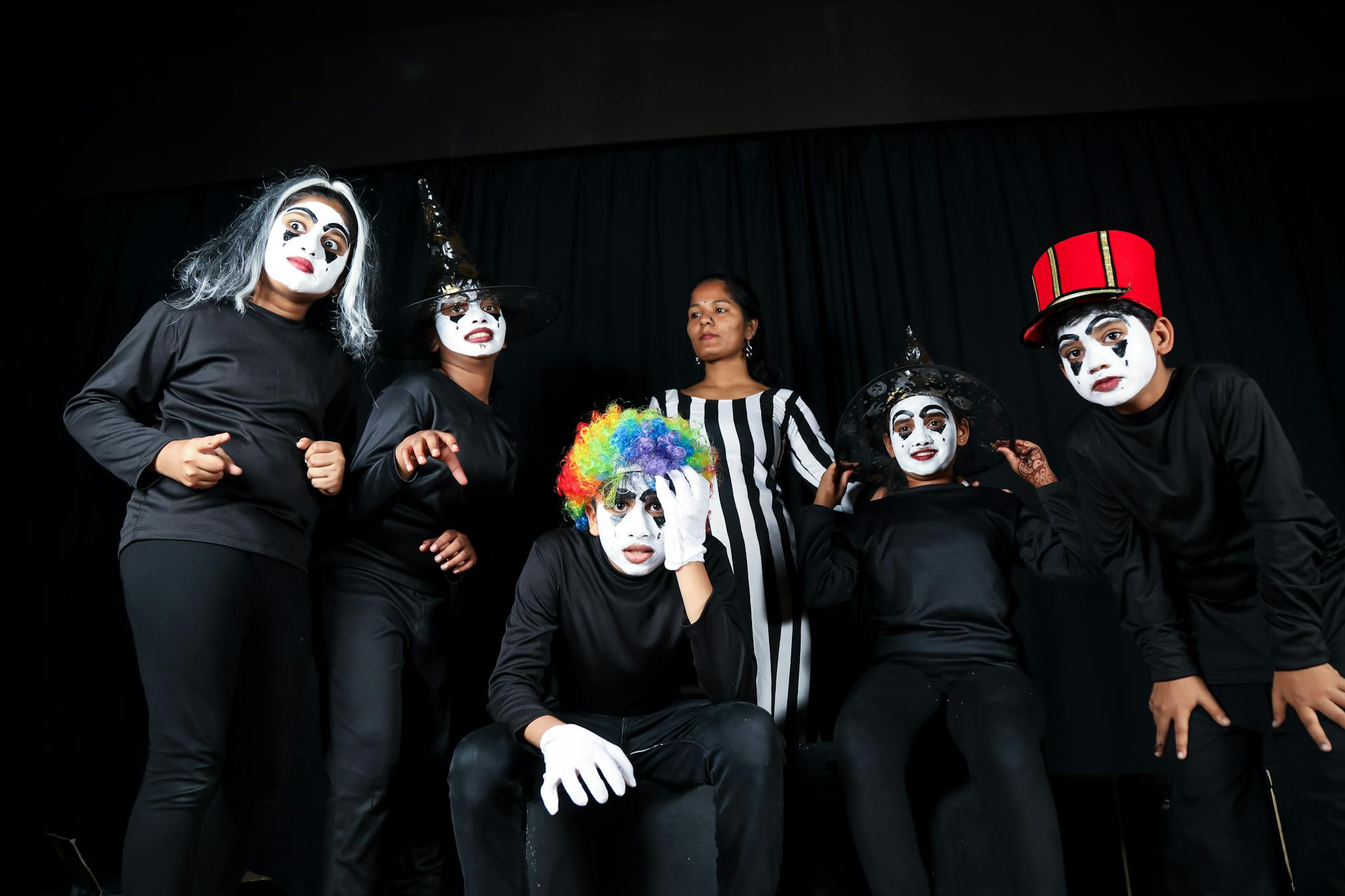 A group of young performers in vibrant costumes and masks showcasing a theatrical performance indoors.