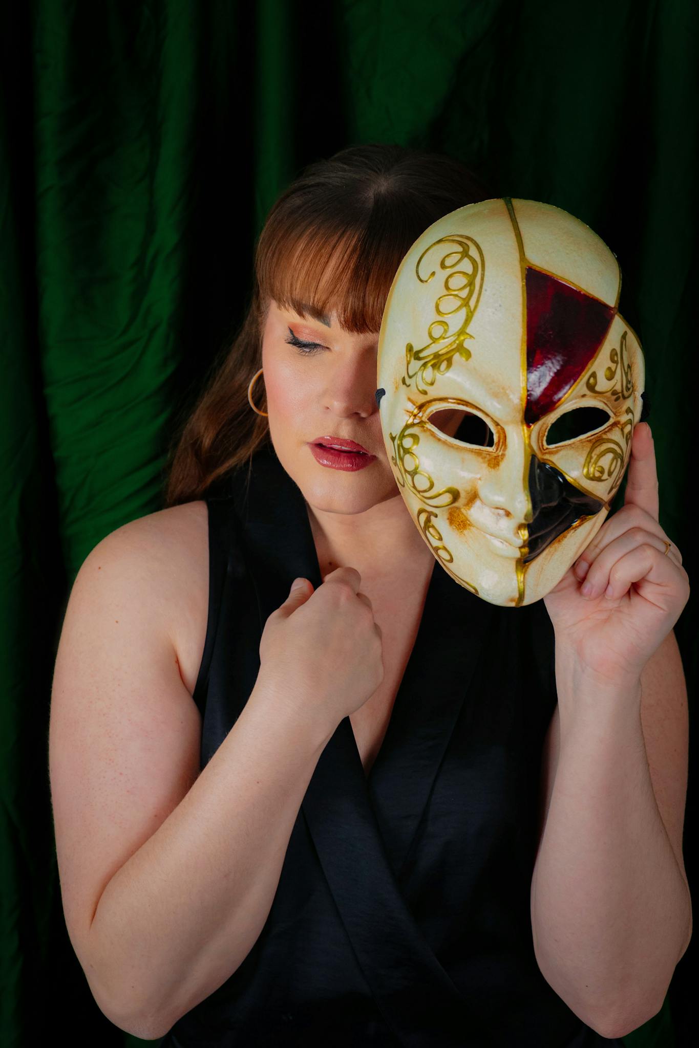 A woman holding a decorative masquerade mask showcases elegance and mystery in a dramatic portrait.